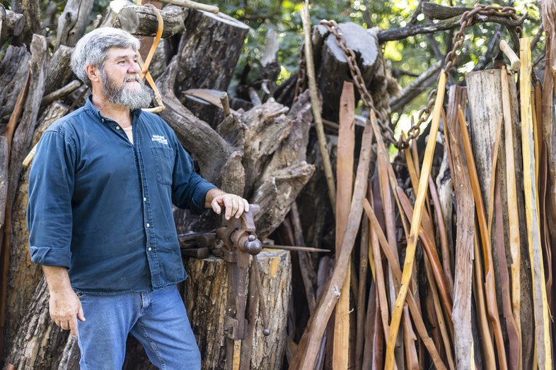 Person standing next to tools on a stump with strips of wood for bows off to the side.