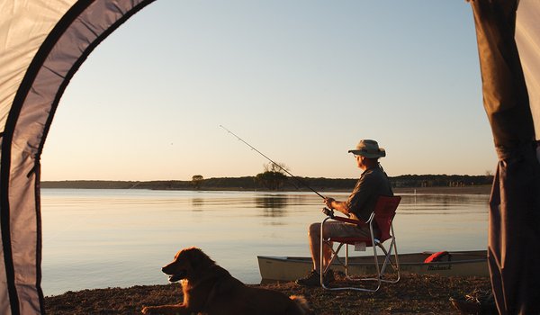 A man fishing on a lake with dog beside him