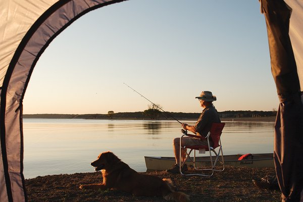 A man fishing on a lake with dog beside him