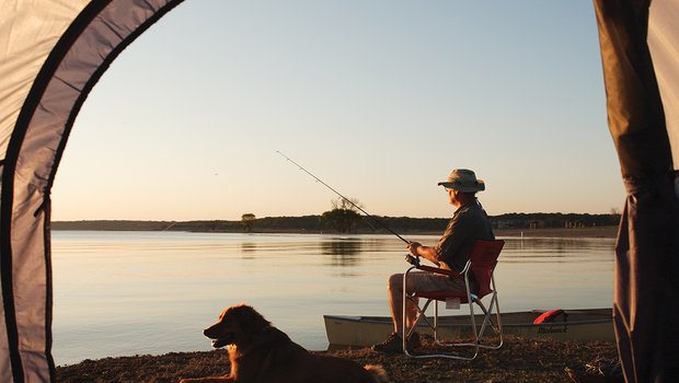 A man fishing on a lake with dog beside him