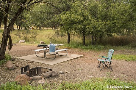 picnic table on a concrete slab with a fire pit nearby and a camping chair