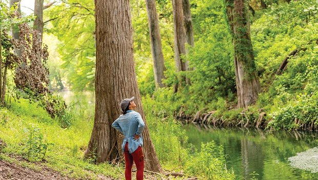 A woman stands by a river looking up
