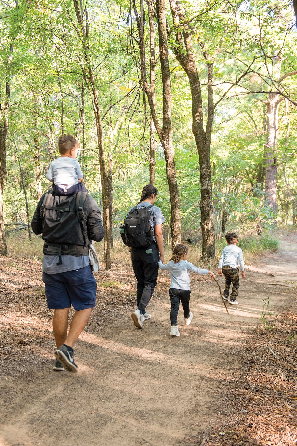 A family with three young kids walking a trail. The youngest is on the father's shoulders.