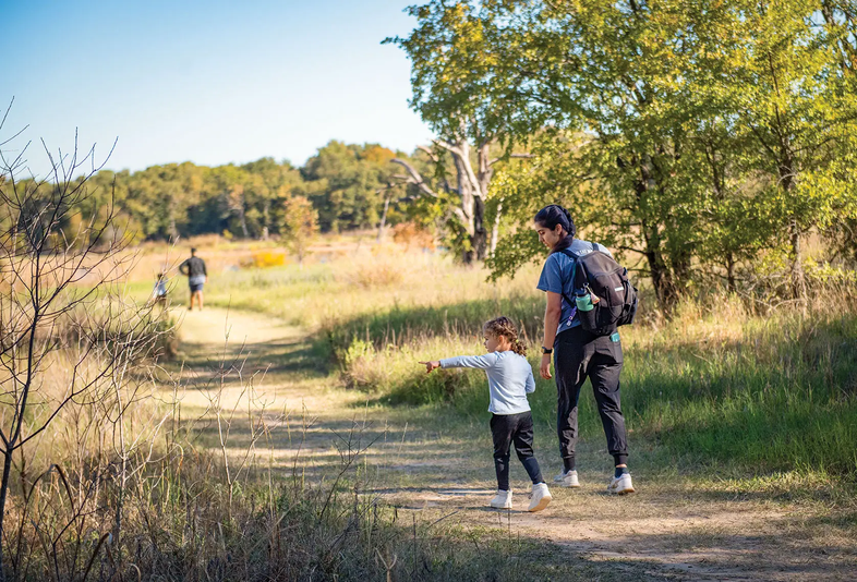 family hiking through a field leading to a wooded area