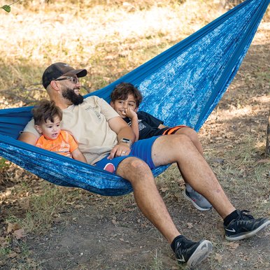 Adult with two young children sitting in a blue hammock between two trees