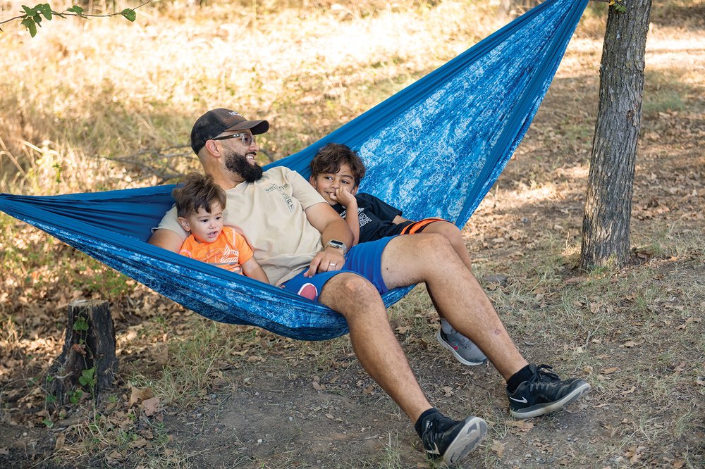 Adult with two young children sitting in a blue hammock between two trees
