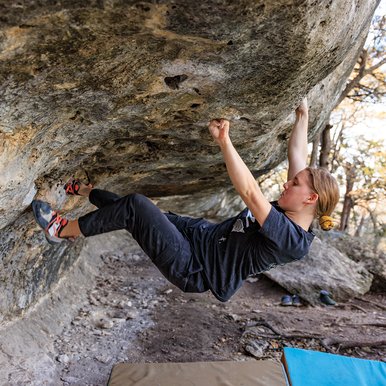 A woman climbing a boulder with two people in background