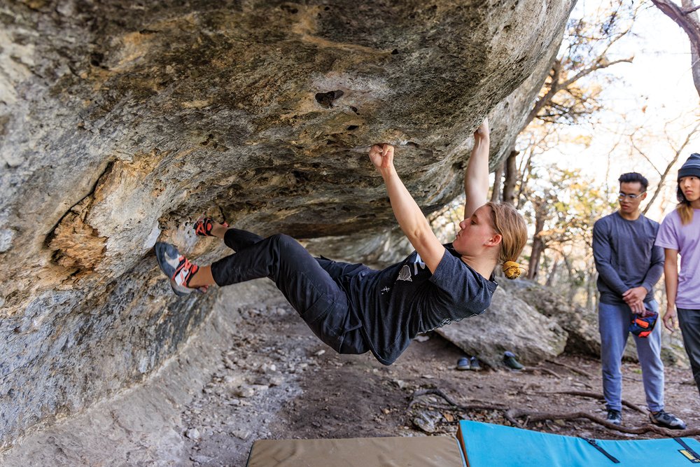 A woman climbing a boulder with two people in background