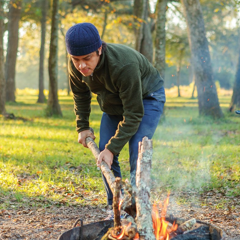 A man stokes a campfire with a tree branch