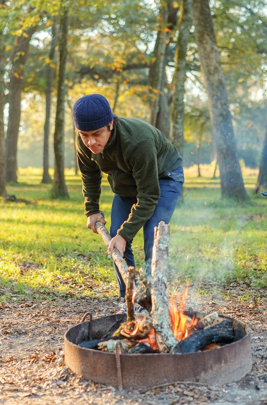 A man stokes a campfire with a tree branch