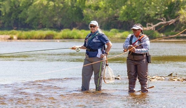 Two people fly fishing in ankle deep water.