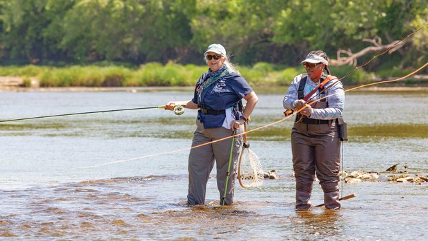 Two people fly fishing in ankle deep water.