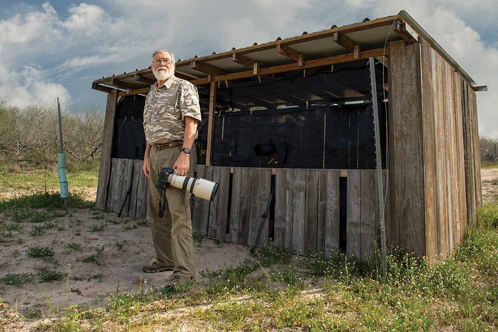 Hugh Lieck a photographer stands next to a hunting shack