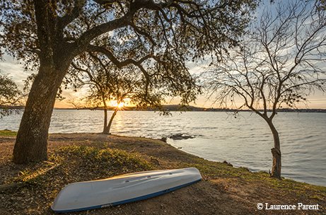 overturned white canoe next to a tree by inks lake while the sun sets