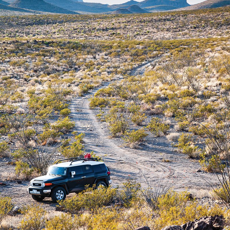 An SUV sits at the end of a dirt road in an arid wilderness area