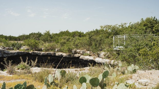 sinkhole surrounded by brush and cacti