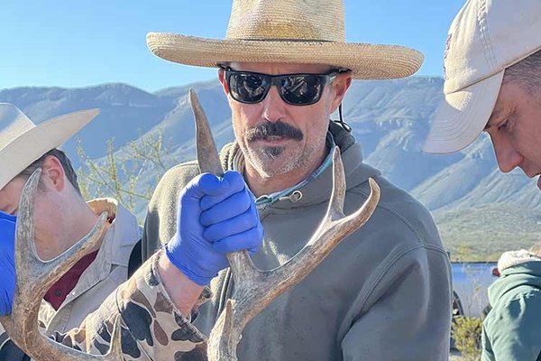 Kevin Legrow In a tan cowboy hat helping other TPWD staff with an orange blindfold and a tag that reads 19