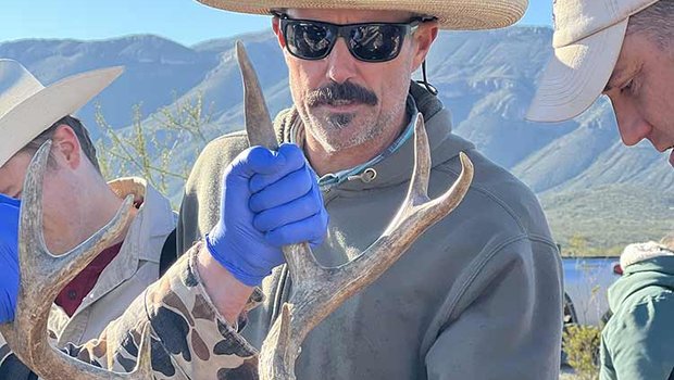 Kevin Legrow In a tan cowboy hat helping other TPWD staff with an orange blindfold and a tag that reads 19