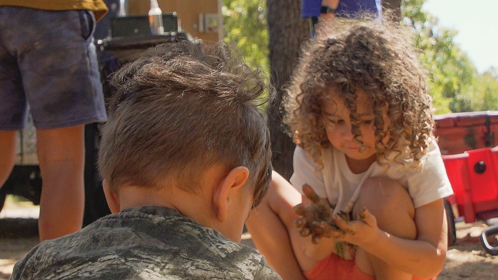 kids squatting while playing in the dirt while camping