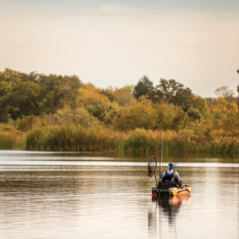 man in a small boat on a lake fishing with the fall brush in the background