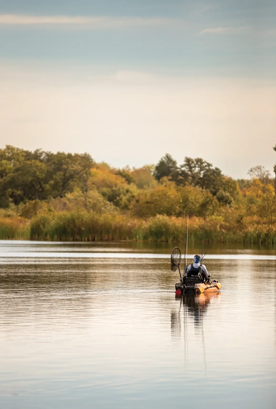 man in a small boat on a lake fishing with the fall brush in the background