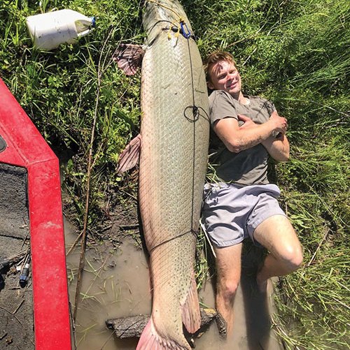 Paul Hefner lies next to an alligator gar he caught