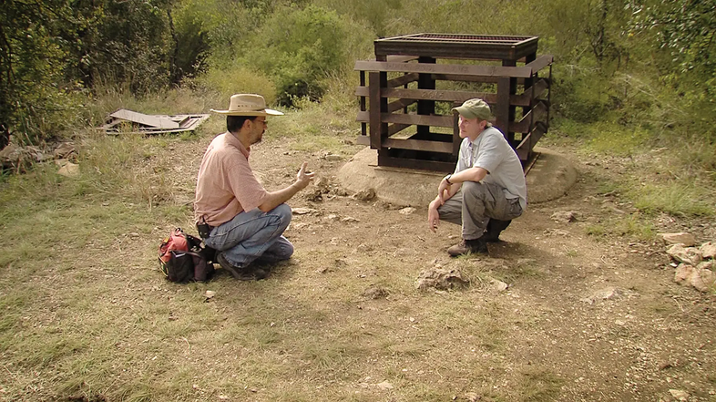 people crouched on the ground talking about ants with a wooden crate behind them