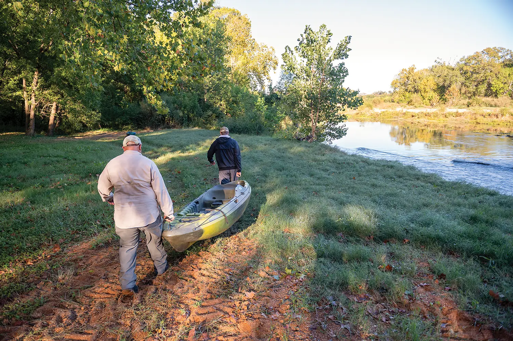 people pulling a kayak toward a river access point