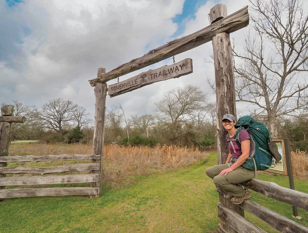 Person sitting on fence under Somerville Trailway Sign
