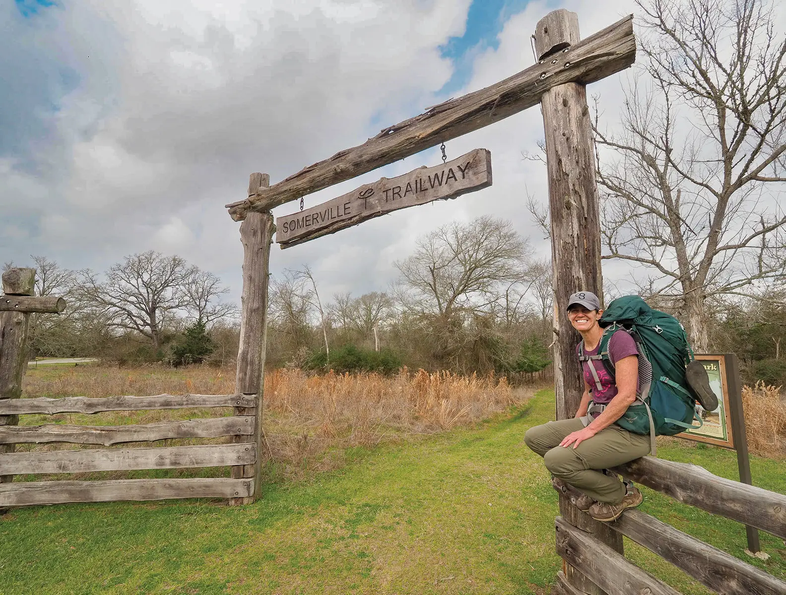 Person sitting on fence under Somerville Trailway Sign