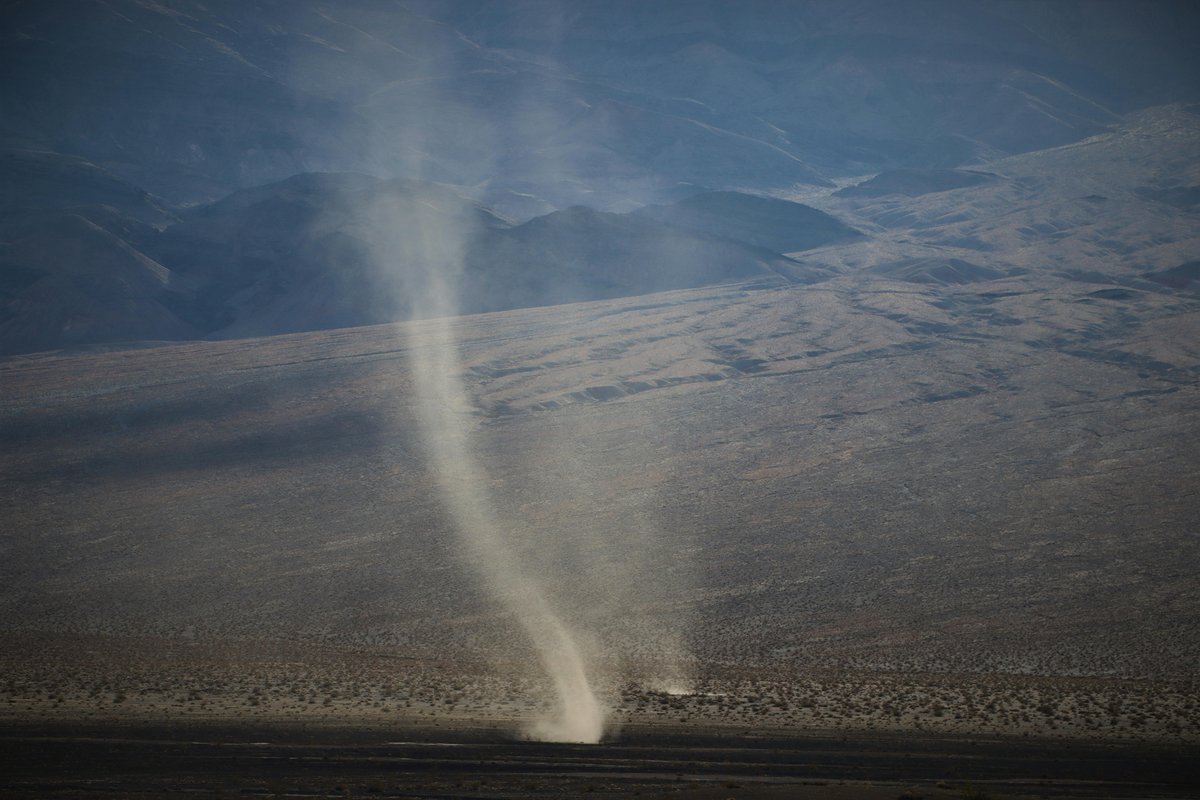 Two Dust Devils next to a road in the desert.