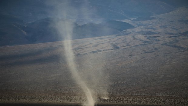 Two Dust Devils next to a road in the desert.