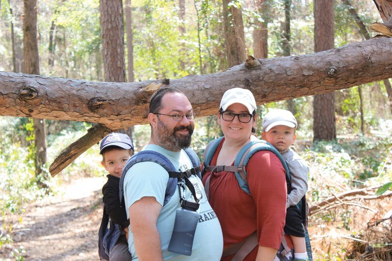 Roberto Family with babies in carriers on their back  looking at the camera with a large fallen limb in the background.