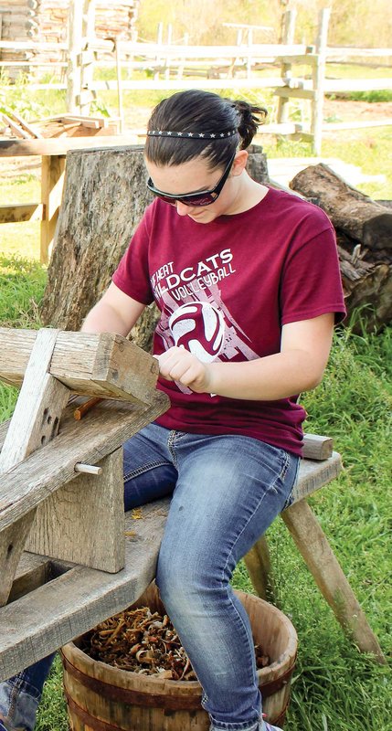 Woman with a red shirt that reads wildcats volleyball sitting on a wooden bench using woodworking tools.