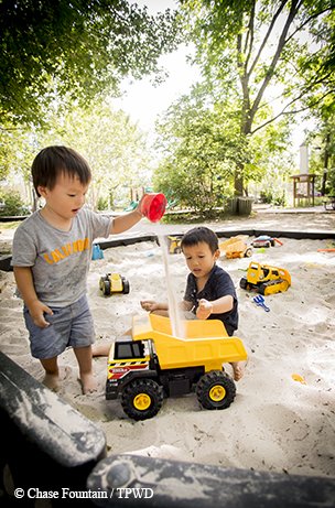 child playing with a sand truck in a natural playscape