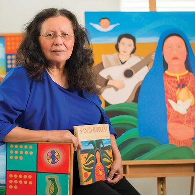 A woman sits with a book titled Santa Barraza