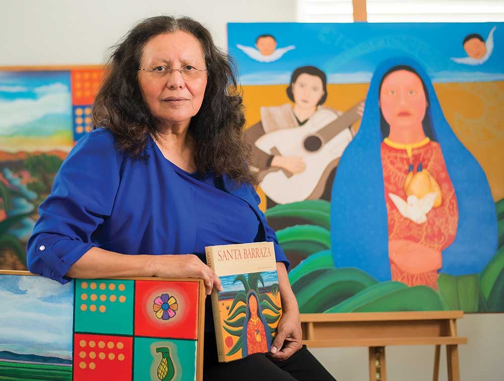 A woman sits with a book titled Santa Barraza