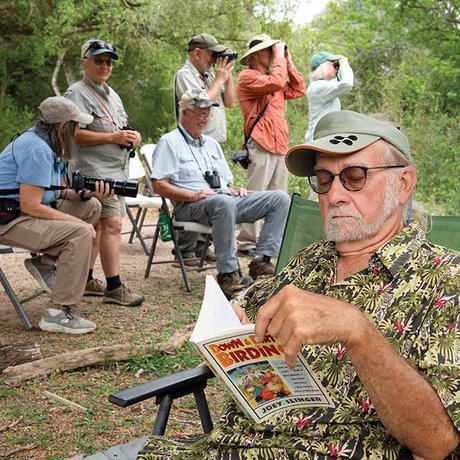 A man reads a magazine with a group of birders behind him