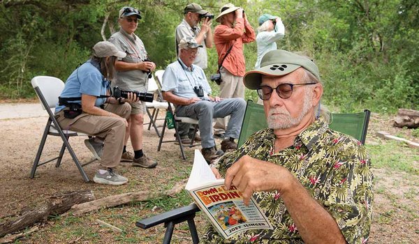 A man reads a magazine with a group of birders behind him