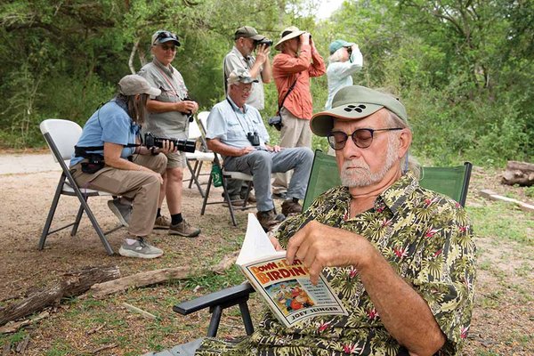 A man reads a magazine with a group of birders behind him
