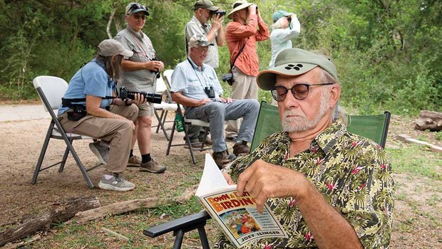 A man reads a magazine with a group of birders behind him