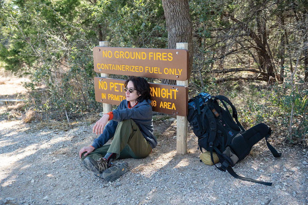 teen resting after backpaking leaning on sign
