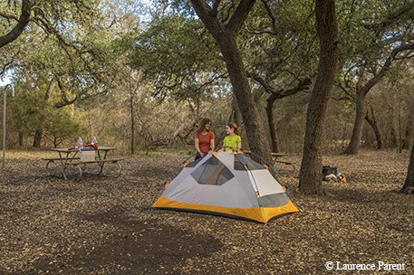 mother and daughter setting up a white and yellow tent in the woods near a picnic table