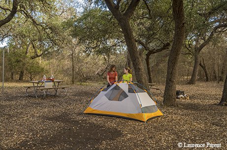 mother and daughter setting up a white and yellow tent in the woods near a picnic table