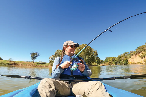 woman fishing from a blue kayak with her paddle across her lap