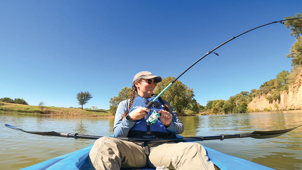 woman fishing from a blue kayak with her paddle across her lap