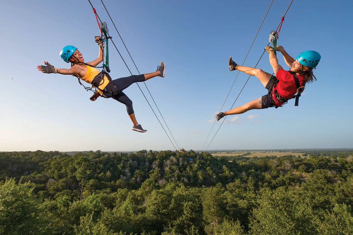 ziplining through the Lost Pines two people on opposite zip lines one in a yellow tank top and one in a red t-shirt