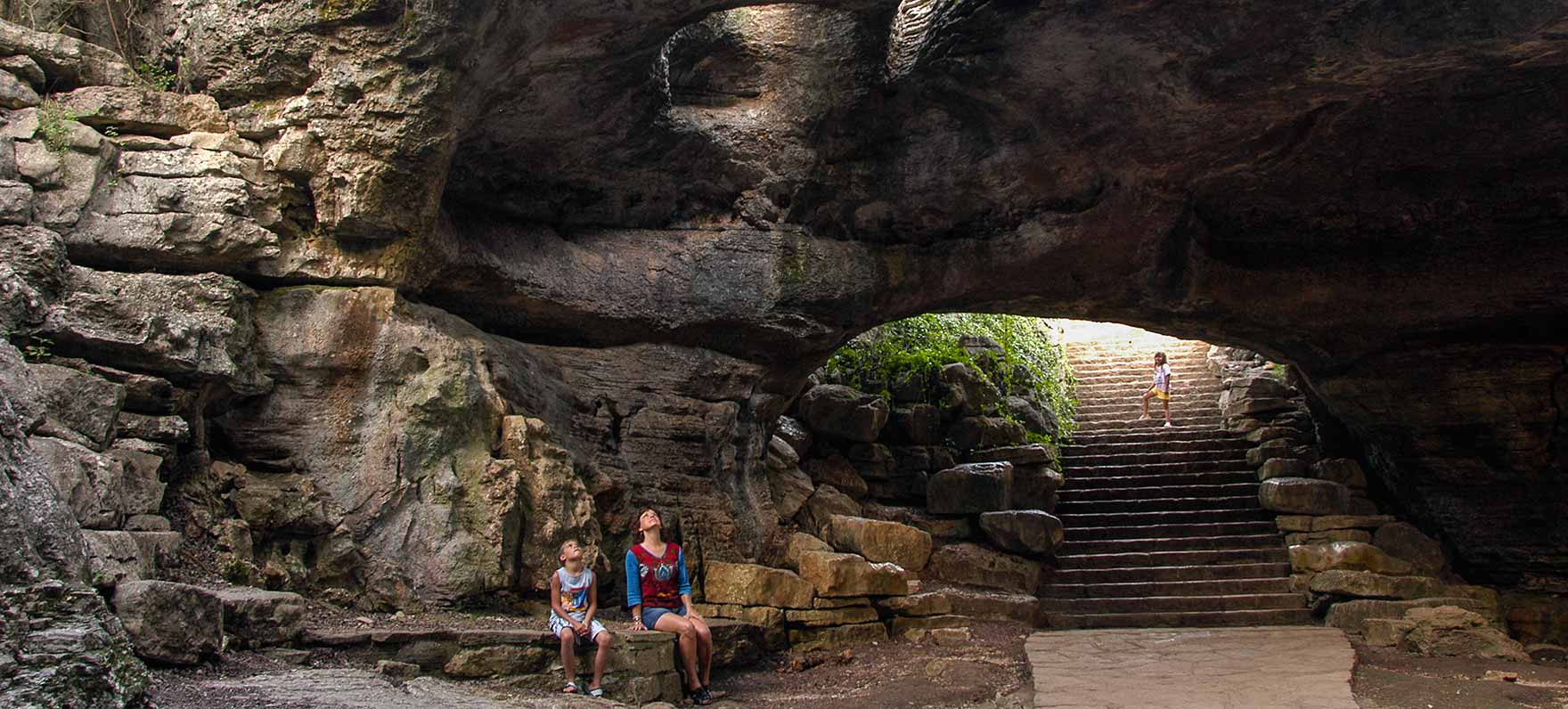 mother and daughter looking up through hole in rock